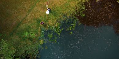 Aerial view of a bride and groom near a lake on green grass.