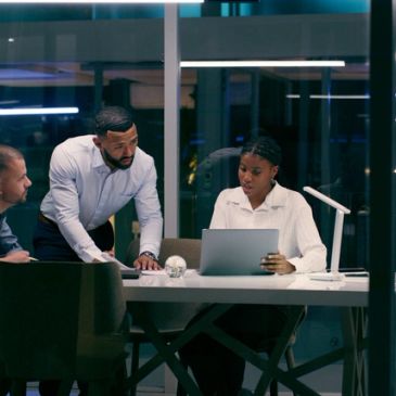 Three professionals collaborating in an office at night.