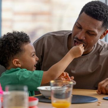 Child feeding father at the table.
