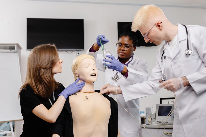 Three medical students practice intubation on a mannequin in a classroom setting.