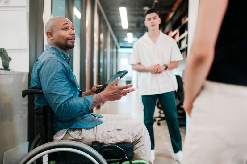 A multiracial group in a shared community workplace discusses a project they are working on.   One man uses a wheelchair.  Shot in Houston, Texas, USA.