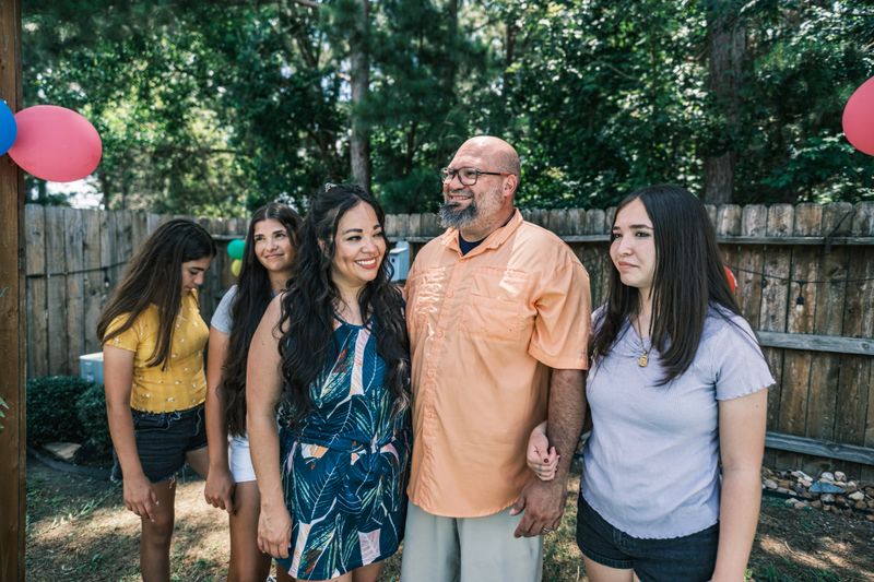 Latino family members taking a break at the backyard party. All dressed in casual summer clothes. Exterior of backyard of private home in Houston, Texas.