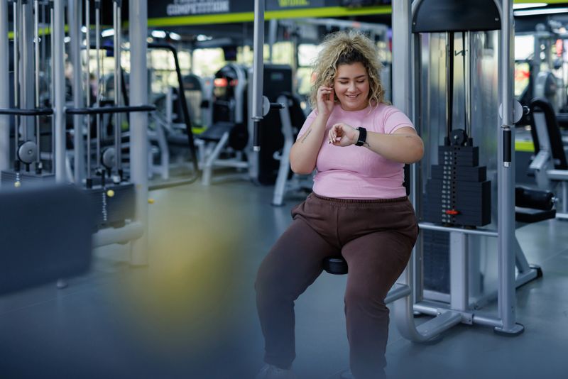 Showcasing the commitment to an active lifestyle, this image presents a woman in a health club setting as she checks her fitness tracker mid-workout, illustrating an involvement in body conscious activities and exercise equipment in the modern gym