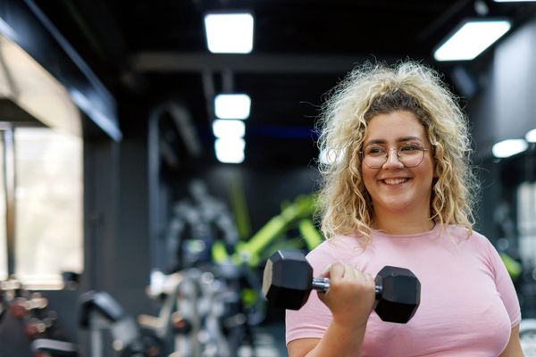 Smiling woman lifting a dumbbell in a modern gym.