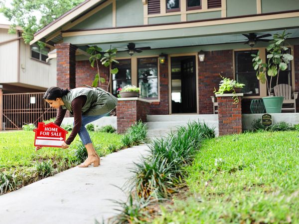 Woman placing a home for sale sign outside a house.