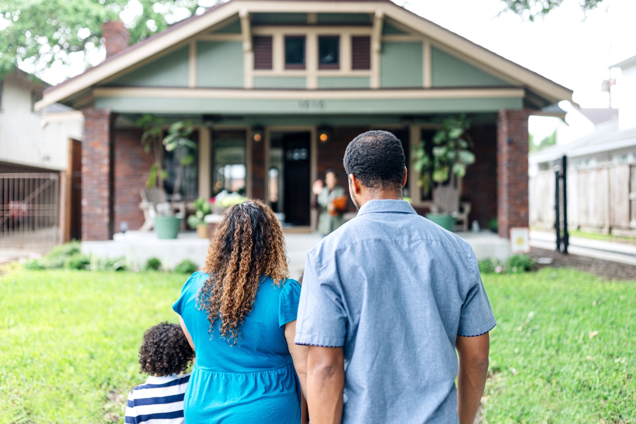 Family standing outside a house, greeting someone at the door.