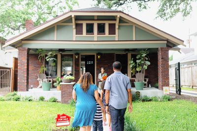 Family walking towards a house for sale with a real estate agent at the door.