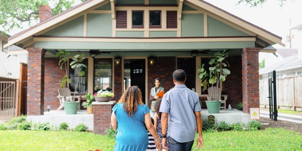 Family walking towards a charming brick house with greenery.