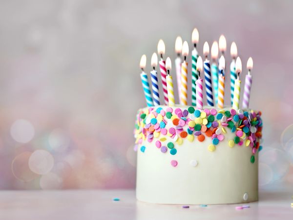 Birthday cake with colorful candles and sprinkles on a pastel background.