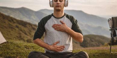 Man meditating outdoors with headphones on, hands on chest and stomach.