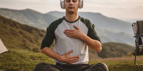 Man meditating outdoors with headphones on, hands on chest and stomach.