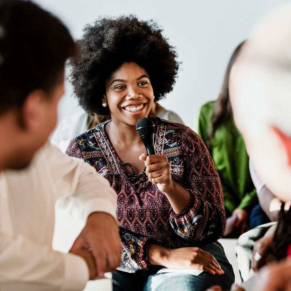 Smiling woman speaking into a microphone during a group discussion.