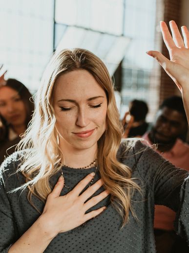 A woman with closed eyes raising her hand and touching her chest, appearing emotional.