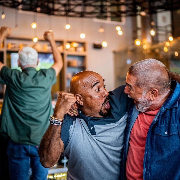 Two men excitedly celebrate while watching a game on TV.