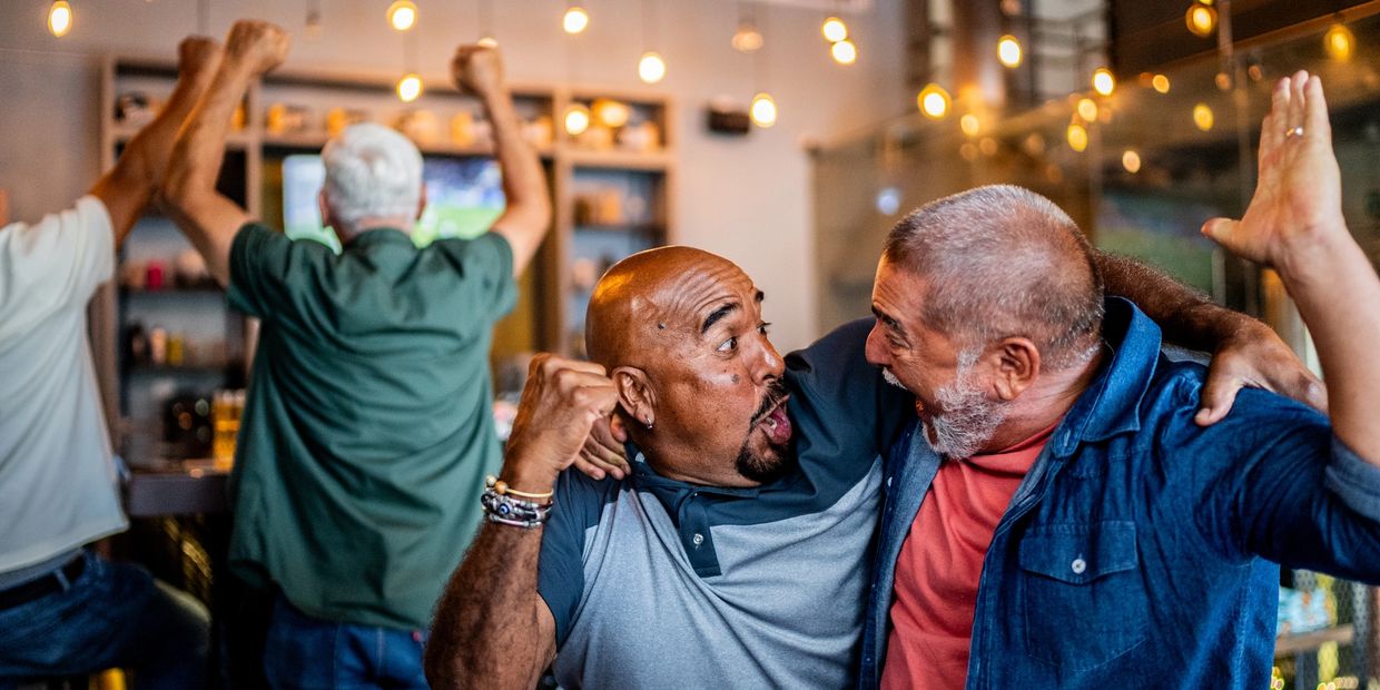 Two men excitedly celebrate a sports event in a lively bar.