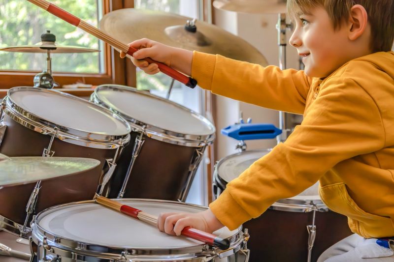 A happy little kid plays drums