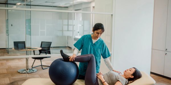 Therapist helping woman with knee exercises using an exercise ball.