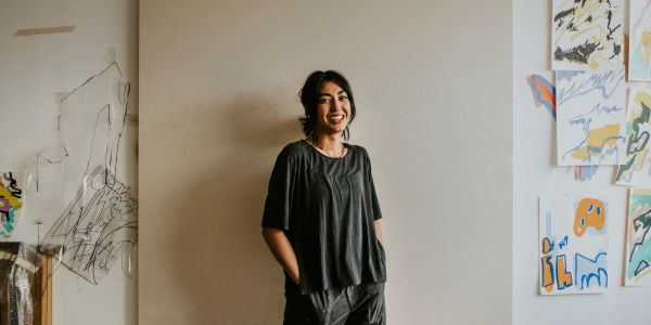 Smiling woman stands in casual outfit against wall with art.