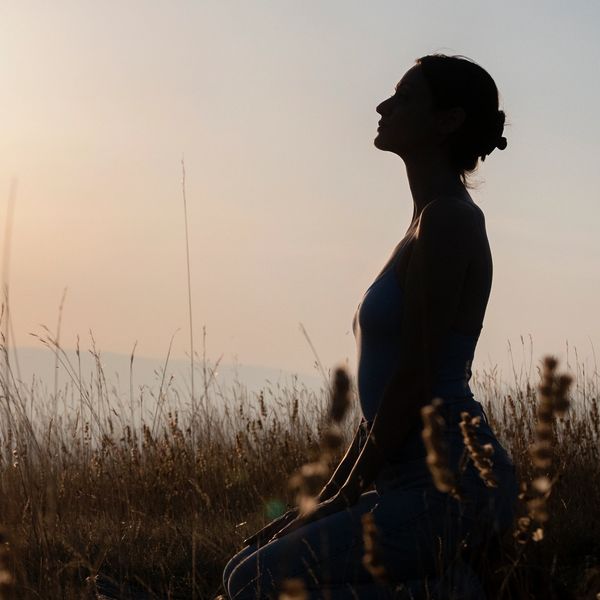 Silhouette of a woman meditating at sunrise in a grassy field.