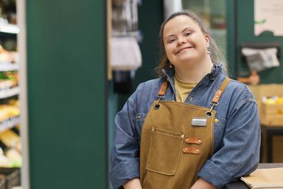 Smiling grocery store assistant in apron at checkout counter.