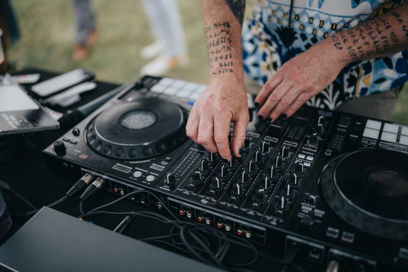 Cropped view of an unrecognizable male DJ playing and mixing music for crowd of happy guests attending wedding reception celebrating marriage of gay couple.