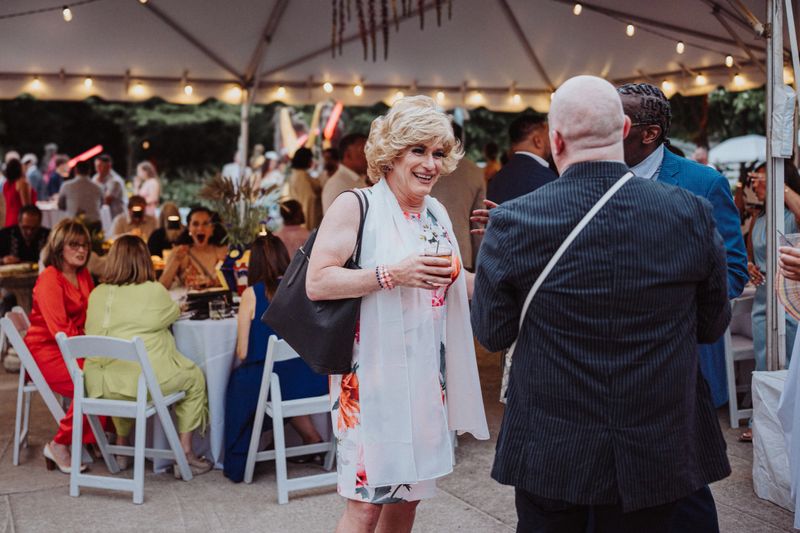A drag queen cheerfully chats with friends while attending the outdoor wedding reception for a gay couple they are friends with.