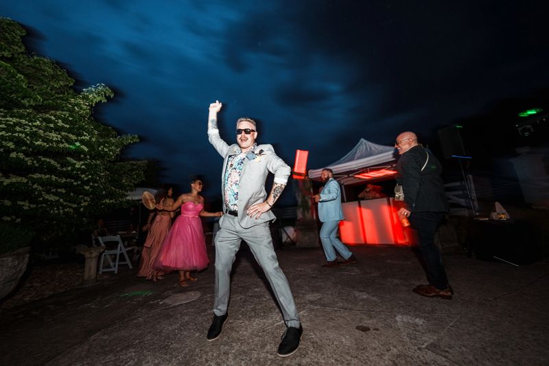 A well-dressed man has fun dancing while attending an outdoor wedding reception at night.