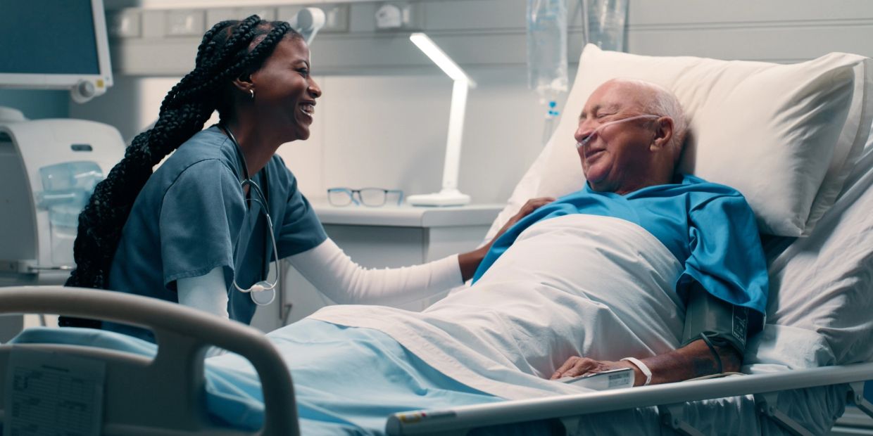 Nurse smiling with elderly patient in hospital bed.