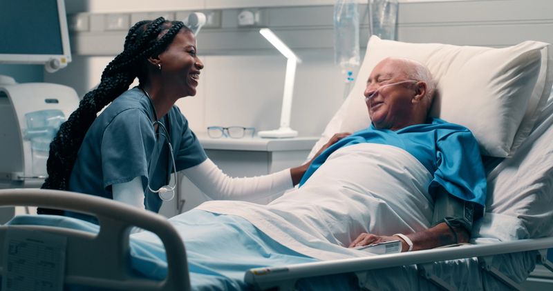 Bed, nurse and smile with patient in hospital for help, support and good news with care. People, professional and happy for healthcare for illness or sickness and recovery with treatment or medical