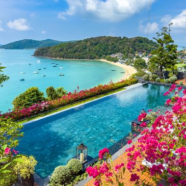 Infinity pool overlooking a turquoise bay with boats and a sandy beach.
