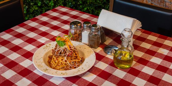 A plate of spaghetti with sauce and cheese on a red and white checkered tablecloth.