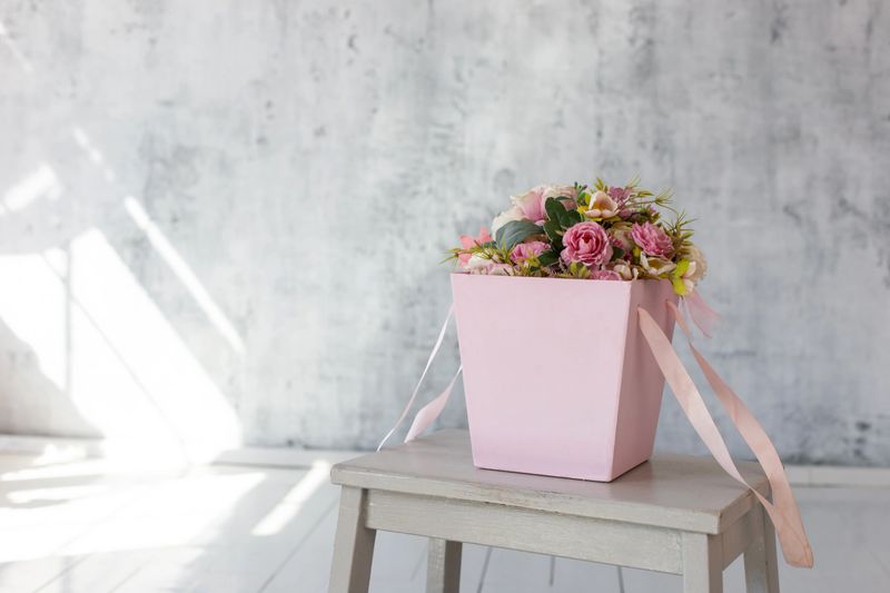 Pink gift paper basket with flowers, standing against a gray wall in an empty room. Copy space. Mock up