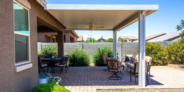 Outdoor patio with seating and a covered roof in a sunny backyard.