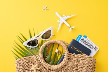 Travel essentials including sunglasses, passport, boarding passes, and a woven bag on a yellow background.