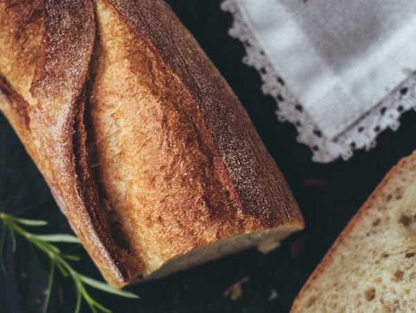 Close-up of crusty baguette bread with herbs and a lace-edged napkin.