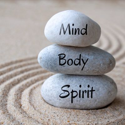 Stacked stones labeled Mind, Body, and Spirit on sand.