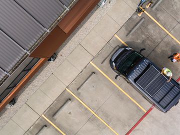 Two workers attach solar panels to a pickup truck in an empty parking lot.