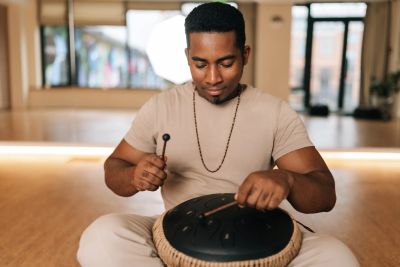 A man playing a handpan drum indoors with focus and rhythm.