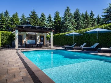 A serene backyard pool with lounge chairs and umbrellas under clear blue sky.