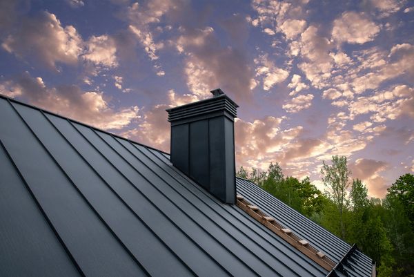 Modern metal roof with chimney under a colorful sky at sunset.