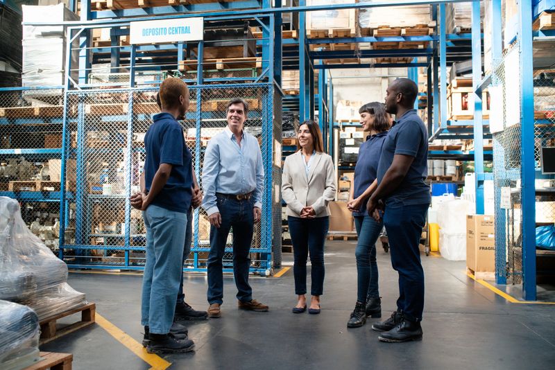 Full length of female manager discussing operations with logistics team. Warehouse supervisor meeting over delivery schedule with group of workers.