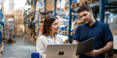Two professionals discussing documents in a warehouse setting.