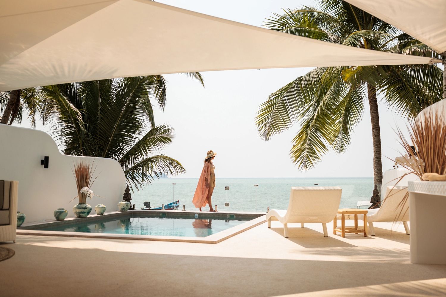 Woman relaxing by a serene beachside pool under palm trees.