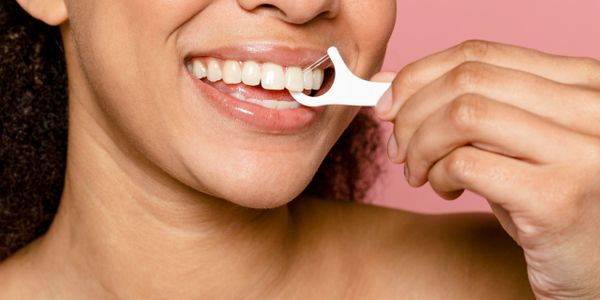 A person flossing their teeth with a white floss pick against a pink background.