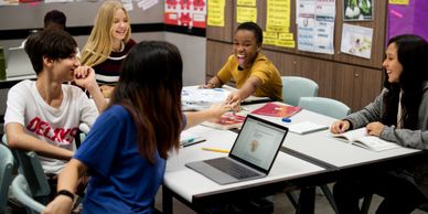 A group of students laughing and interacting during a study session in a classroom.