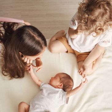 Two kids interacting with a newborn baby on a bed.