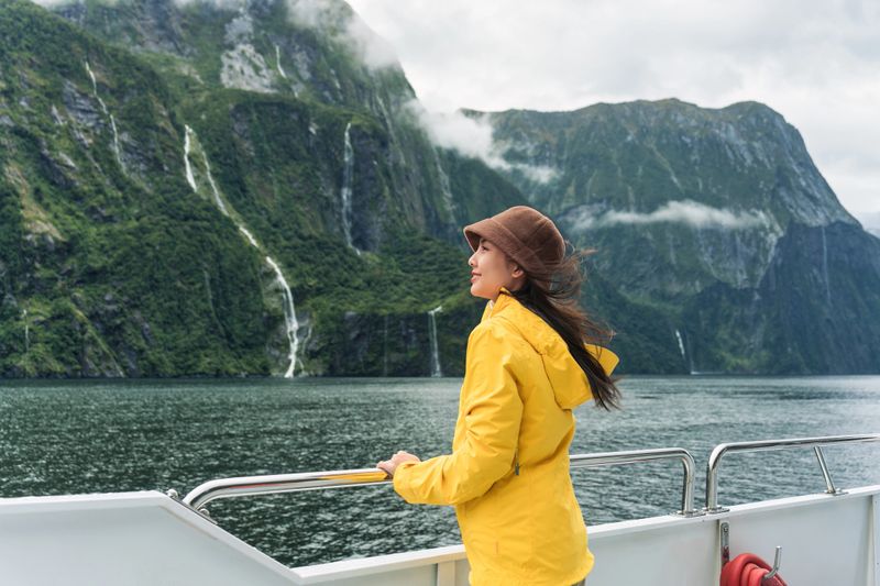 Young asian woman enjoying the view of Milford Sound during ferry cruise on vacation at Fjordland national park, New Zealand