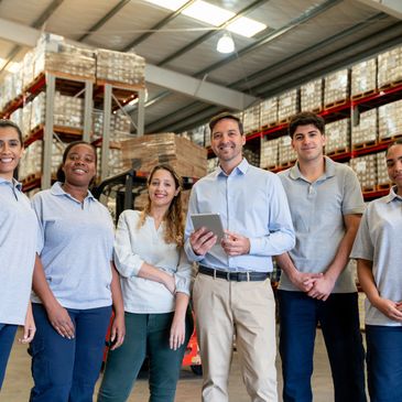 Diverse warehouse team smiling and posing for a group photo inside a large storage facility.