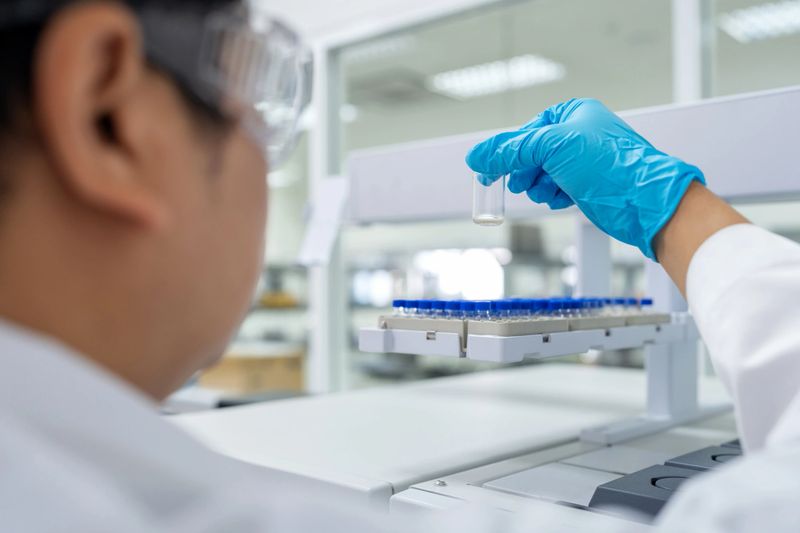 A dedicated researcher, clad in a lab coat and protective goggles, stands in front of a sophisticated Gas Chromatography-Mass Spectrometry (GC-MS) machine. With precision, the scientist picks up a sample vial and carefully places it into the tray of the GC-MS equipment to analyze the composition of the sample.