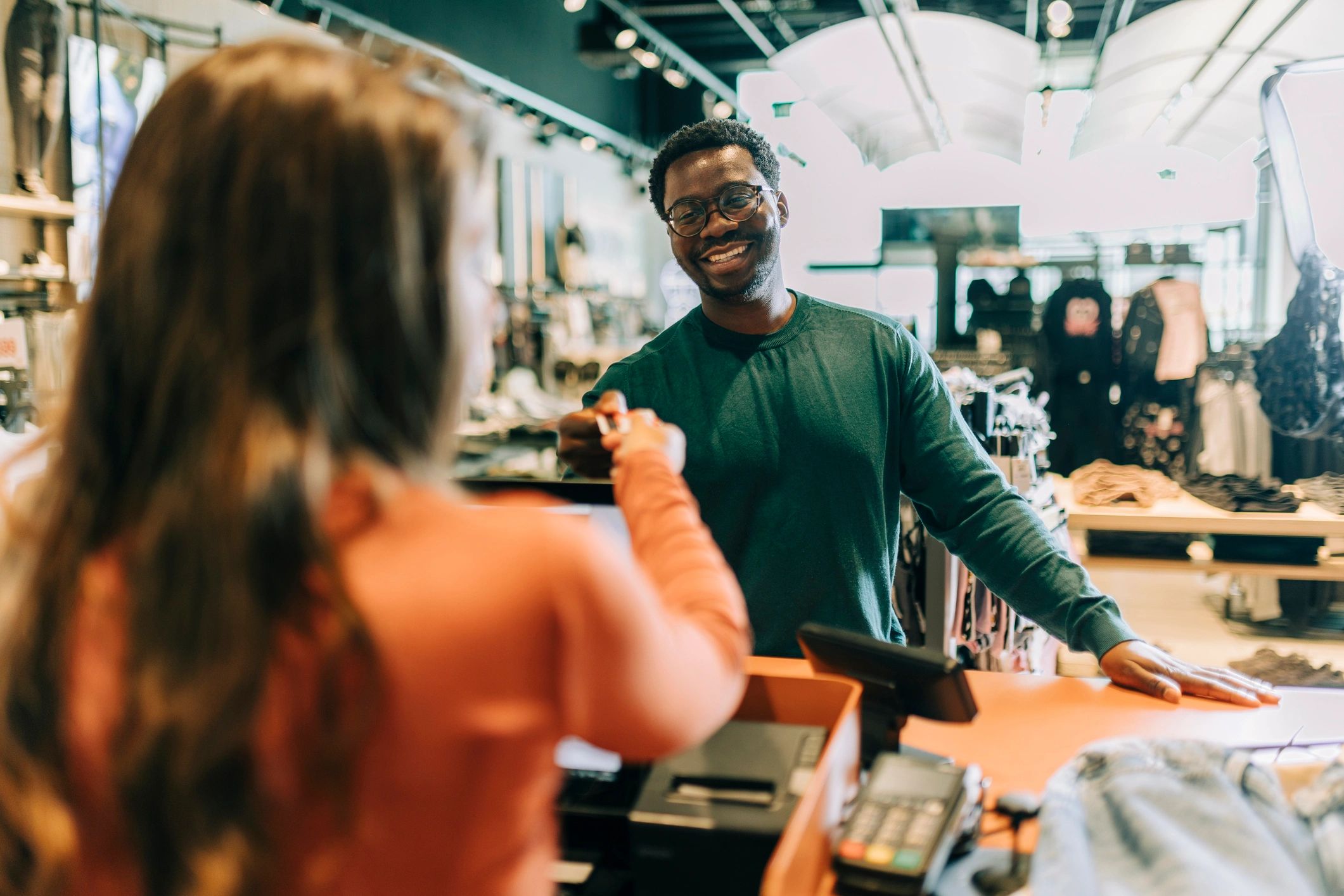 A man smiling while paying at a store counter.